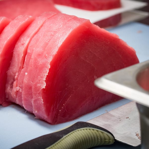 Freshly sliced, vibrant red tuna steaks on a light blue cutting board, ready for Grindz poke.