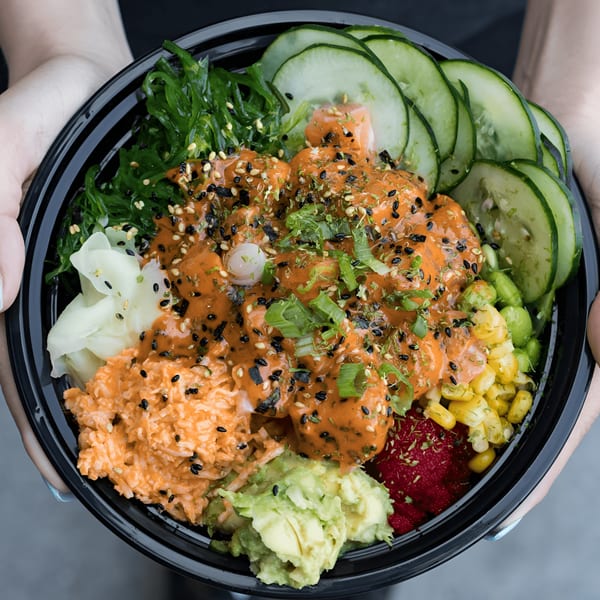 Hands holding a Grindz poke bowl with salmon, seaweed, cucumber, corn, avocado, and ginger.