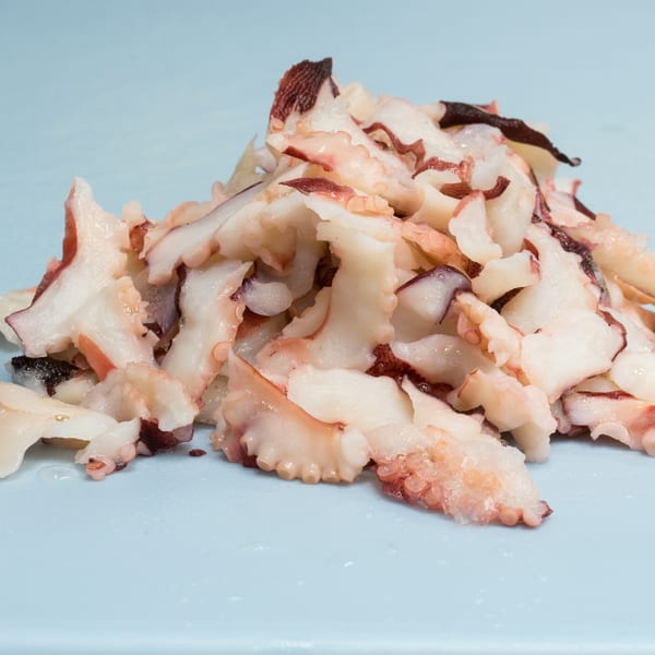 Close-up of a pile of chopped octopus pieces, with white and reddish-brown colors, on a light blue surface.